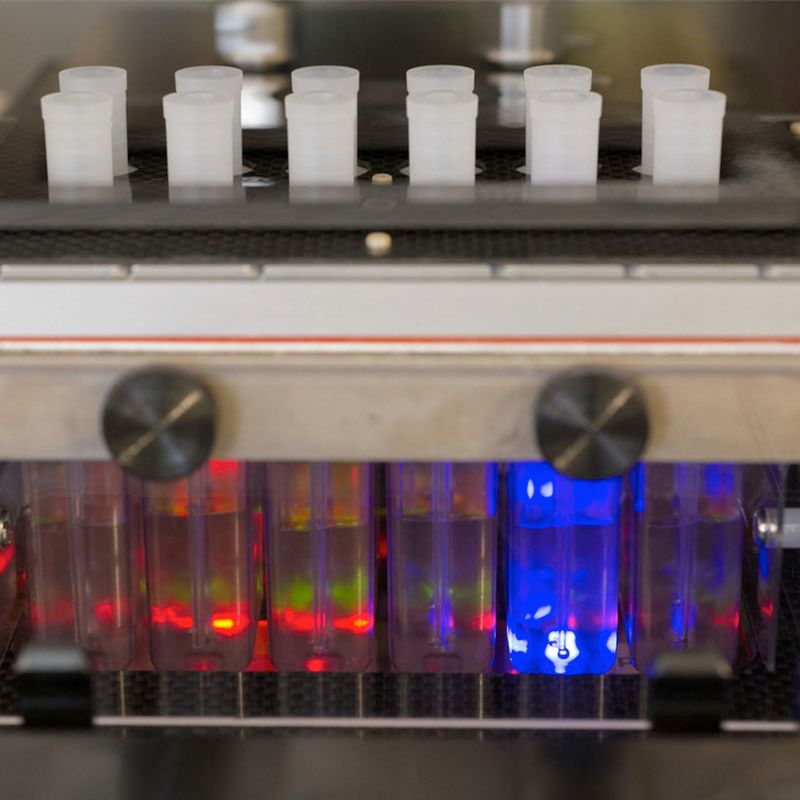 A laboratory device containing multiple test tubes illuminated with red and blue lights for high-throughput sample processing.