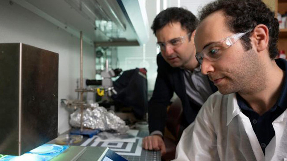 Researchers working at a laboratory bench using analytical equipment to examine materials under controlled conditions.
